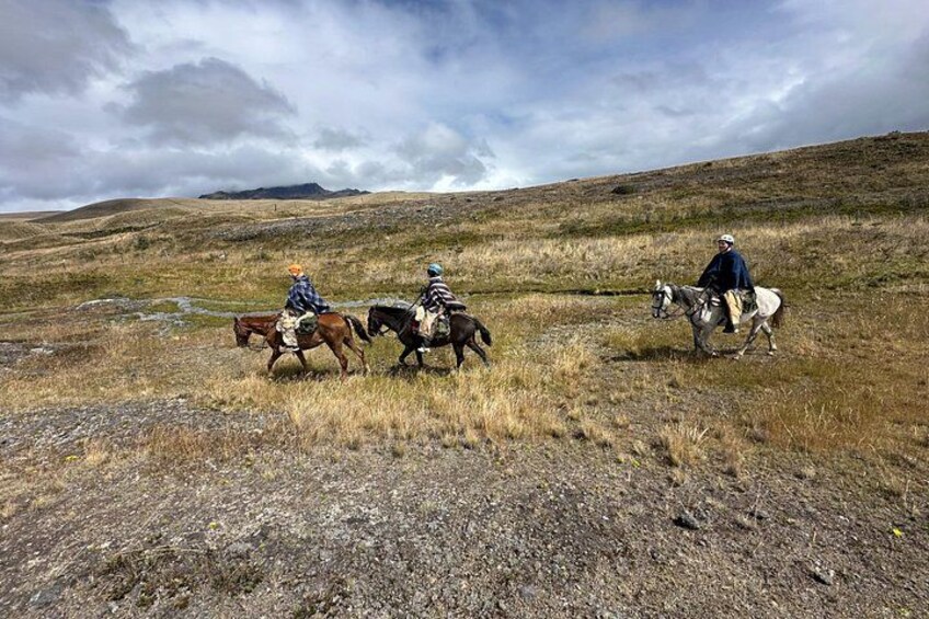 Three people riding horses across a grassy field with hills in the background. 5