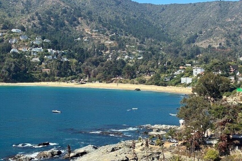 A coastal landscape with a beach, boats, and houses on a hillside. 1
