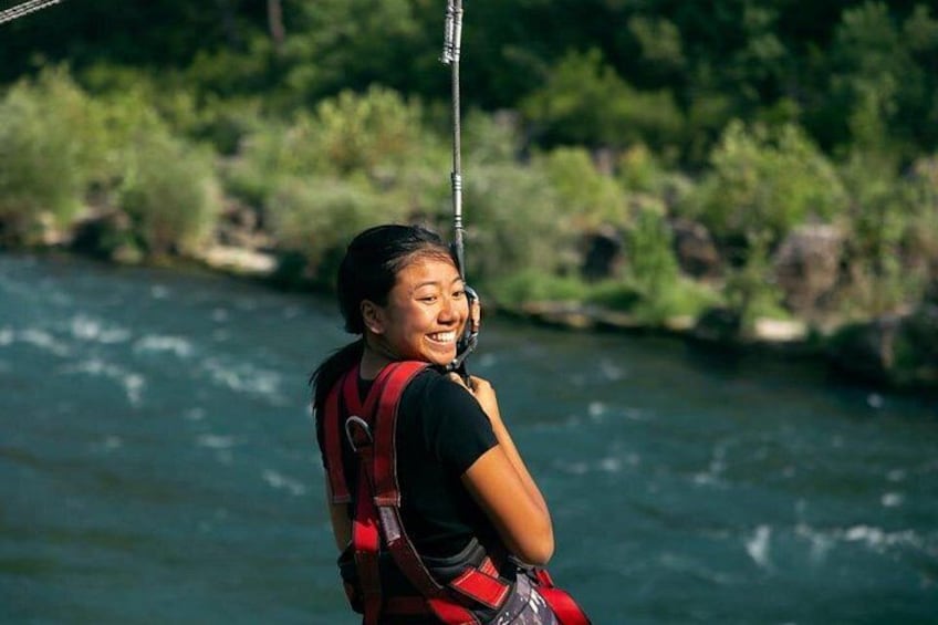 En person åker på en zipline över en flod med grönskande vegetation i bakgrunden. 5