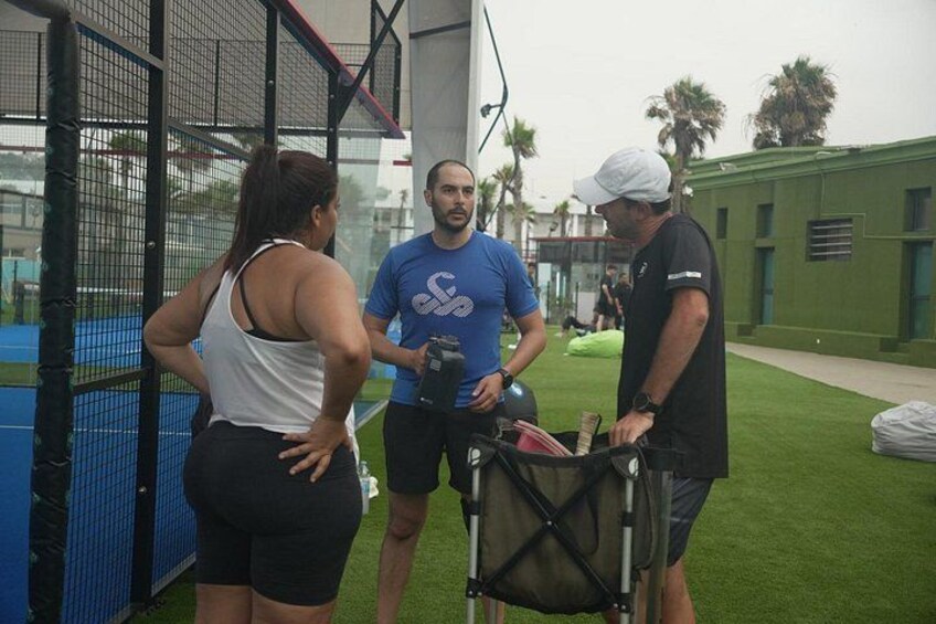 Three people standing outdoors near a sports facility with a netted enclosure and a green field. 4