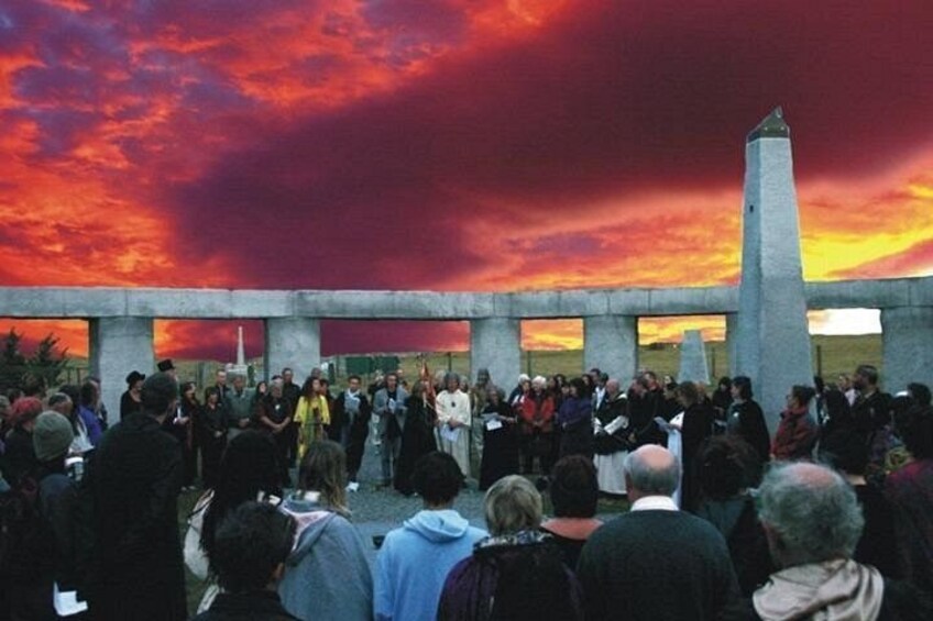 Un groupe de personnes s’est rassemblé autour d’un monument, avec un coucher de soleil spectaculaire en arrière-plan. 3