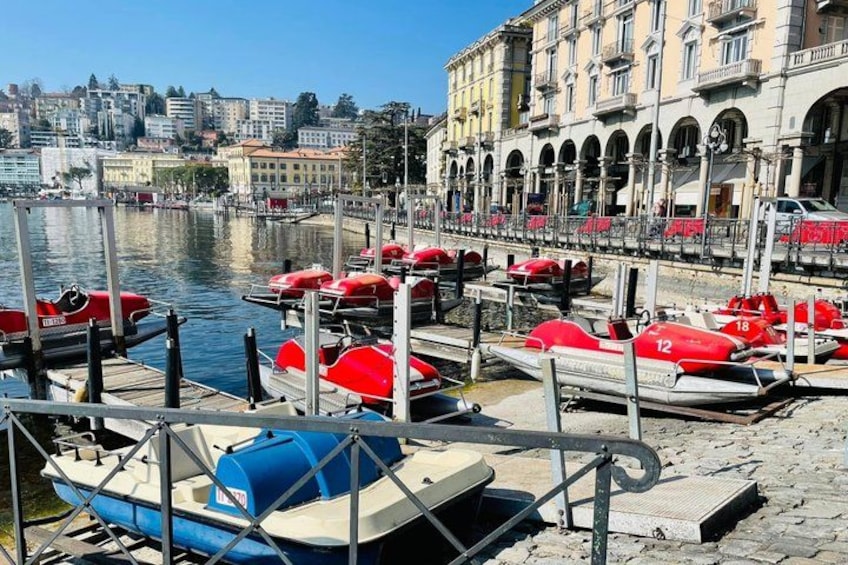 Un puerto deportivo con barcos rojos y azules amarrados, un edificio frente al agua y un paisaje urbano al fondo. 2