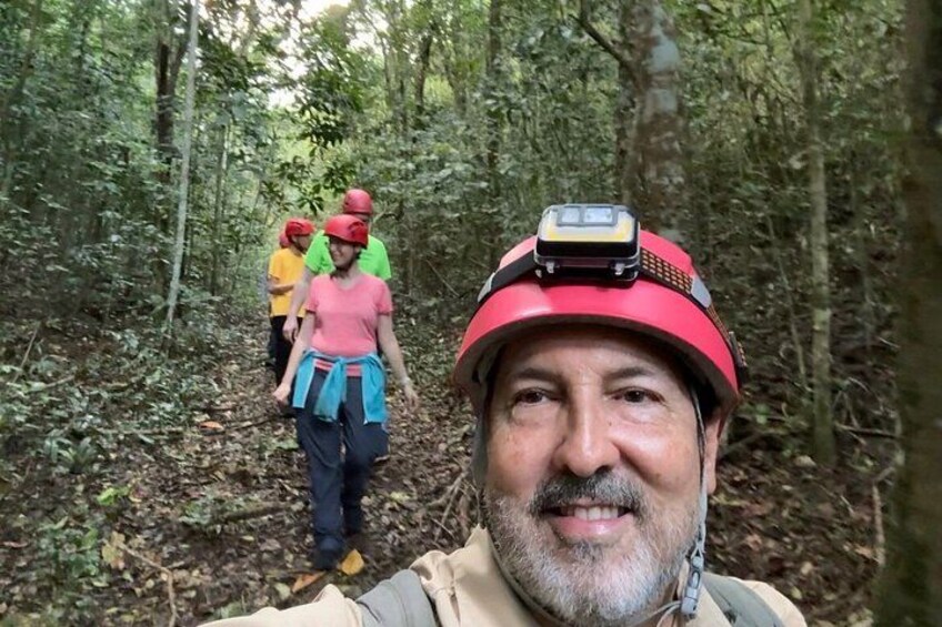 A forested area with a person wearing a red helmet and a device on their head, and another person in a pink shirt and blue shorts. 2