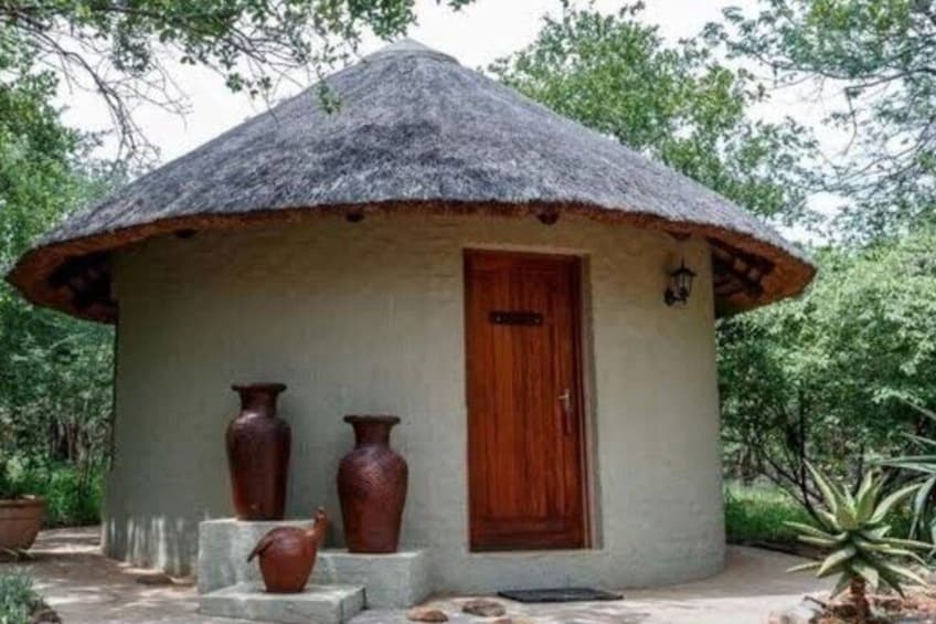 A thatched-roof hut with a wooden door, surrounded by potted plants and large vases. 3