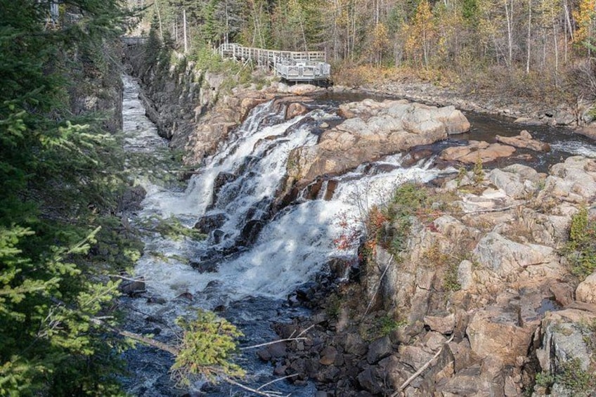 A waterfall cascading over rocks, surrounded by trees and a wooden bridge. 2