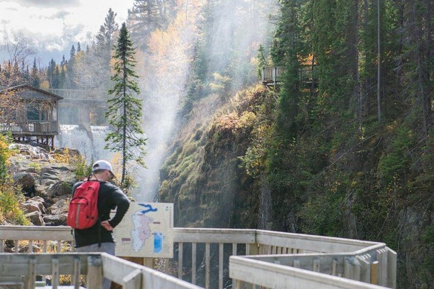 A hiker with a red backpack on a wooden bridge overlooking a forested area with a waterfall. 4