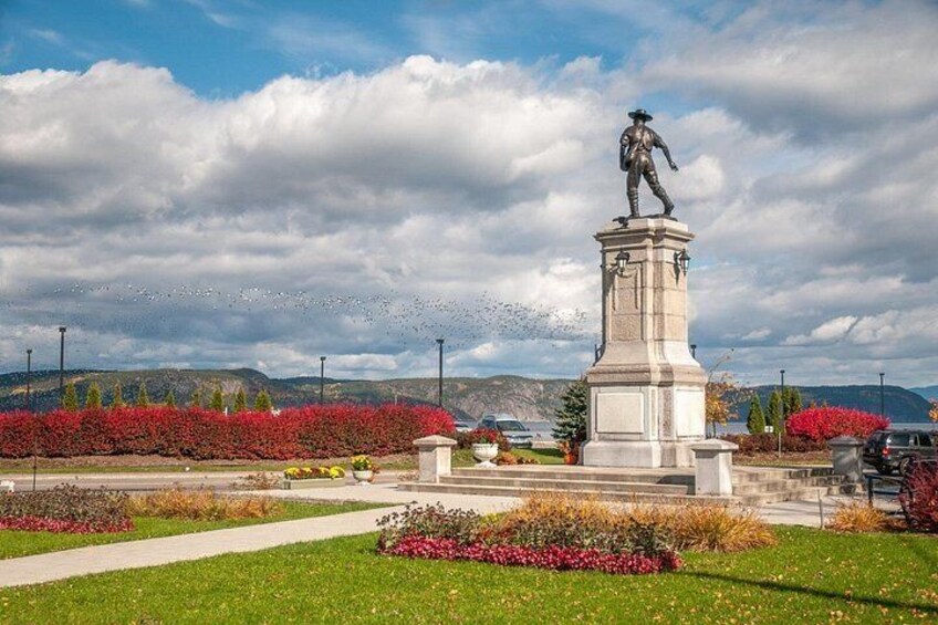 A statue on a pedestal in a park with flower beds and a clear sky. 4