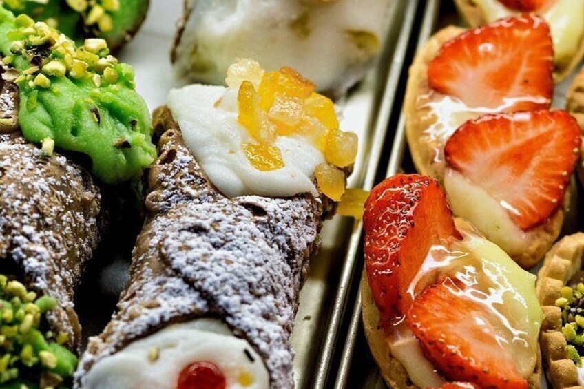 Diverse desserts, waaronder een rolletje met poedersuiker, een taartje met aardbeien en een groen dessert met noten. 1