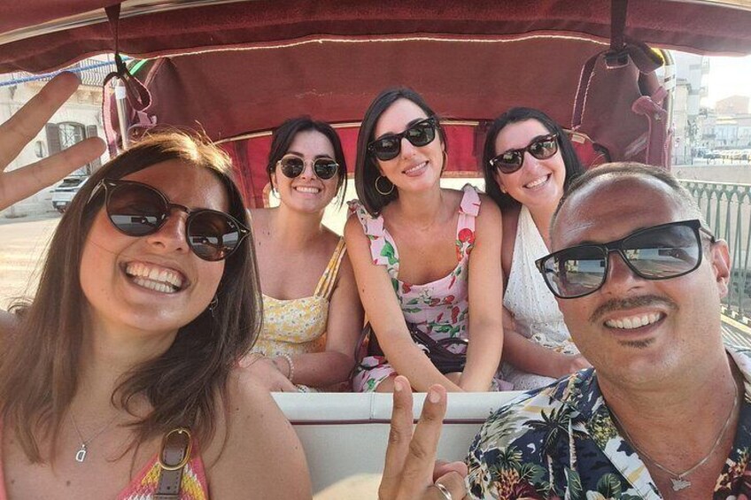 Een groep mensen op een boot met een rood zonnescherm, met een stadsgezicht op de achtergrond en een heldere lucht. 5
