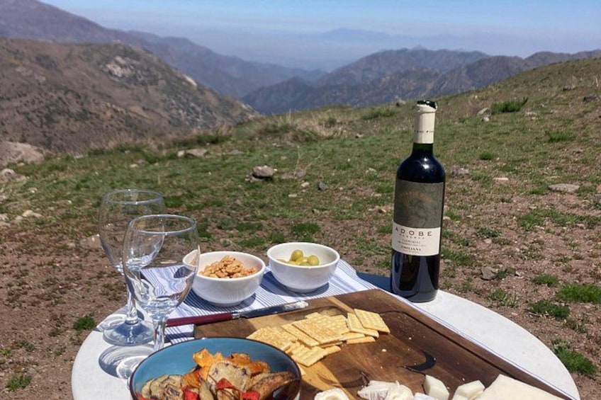 En picknickuppsättning på ett berg med en flaska vin, glas, skålar med mat och en skärbräda. 3