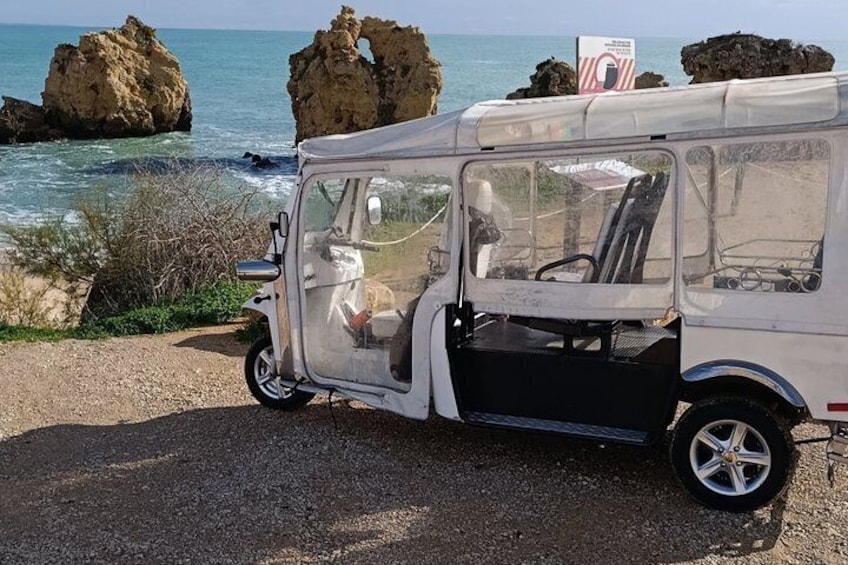 A white van parked by the sea with rocky formations in the background. 1
