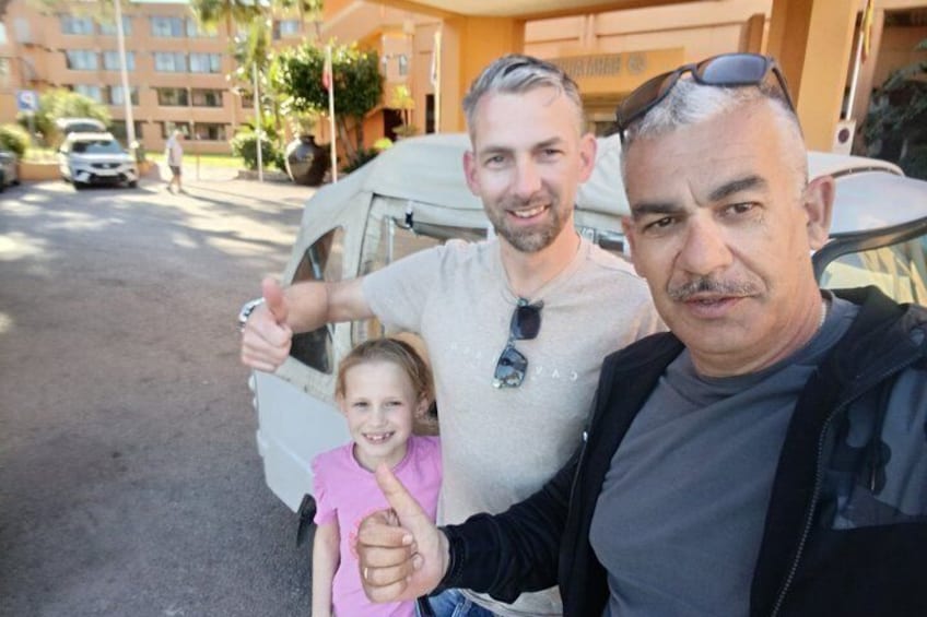 Three people in front of a vehicle with a building in the background. 3