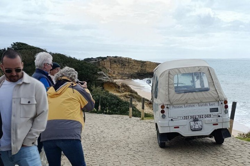 A coastal road with a vehicle labeled 'Passeios Turísticos - Tourist Tours' parked on the side. 2
