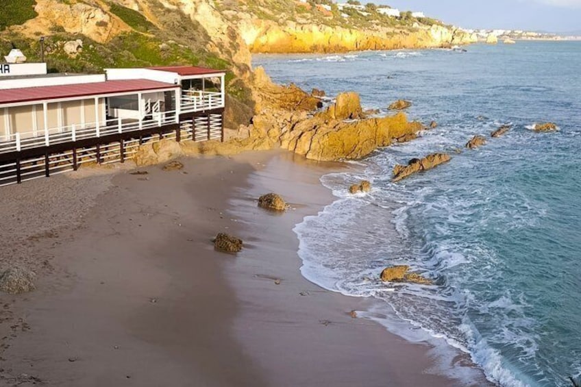 A coastal landscape with a beach, rocky outcrops, and a building with a red roof. 4
