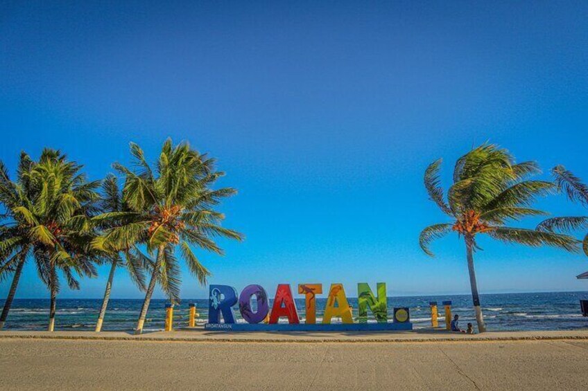 A beach with palm trees and the word "ROATAN" spelled out in colorful letters. 2