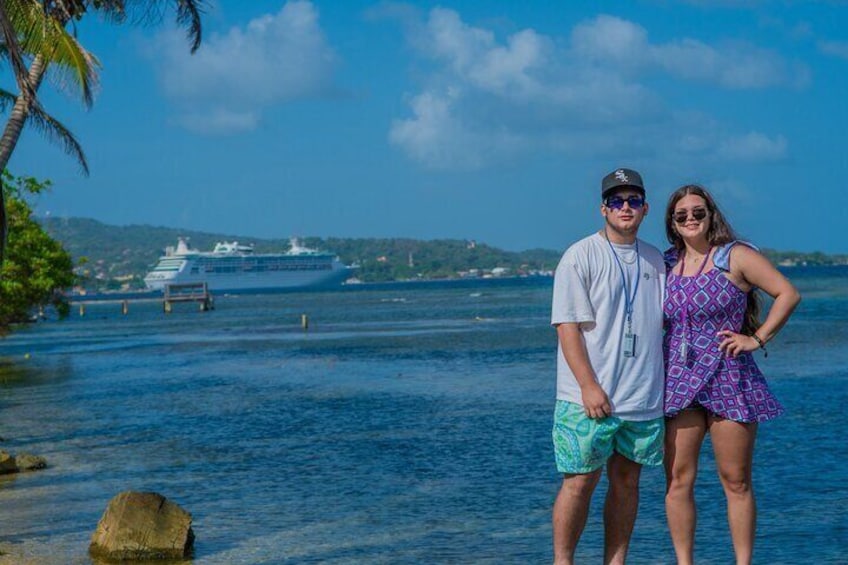 A couple standing by a waterfront with a cruise ship in the background. 1