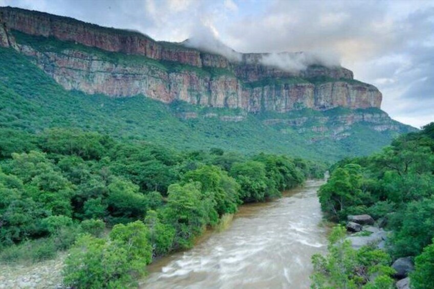 A river flowing through a lush valley with a steep cliff in the background. 4