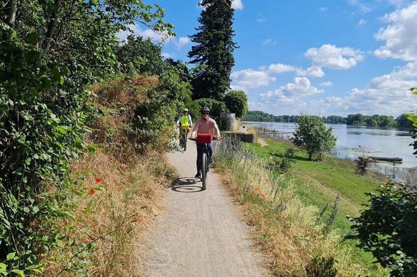 Un chemin pavé longe un plan d’eau, où l’on voit des cyclistes et une personne qui se promène. 2