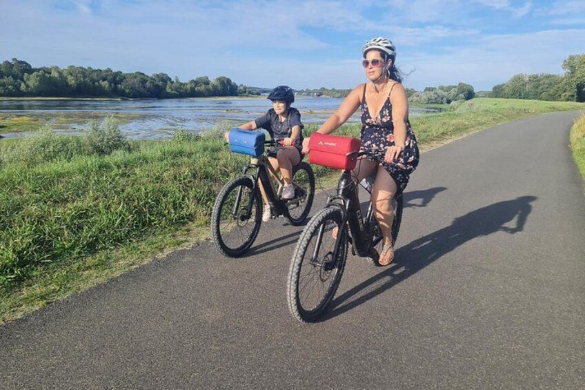 Two people riding bicycles on a paved path with a body of water and greenery in the background. 5