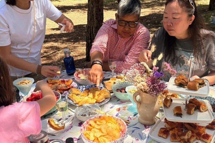 Een groep mensen dineert buiten, met verschillende gerechten en drankjes op tafel. 5