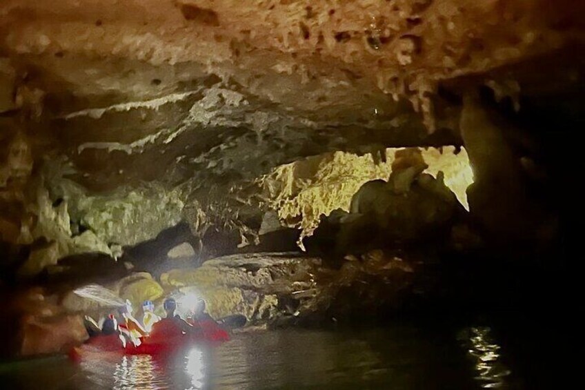 Interior de una cueva con estalactitas y estalagmitas, y una persona remando en kayak sobre el agua. 1