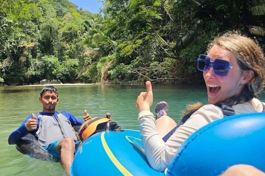 Two people floating on a river in a raft, surrounded by lush greenery. 1