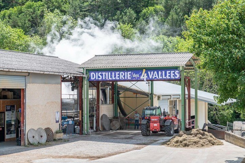 Una destilería con un letrero que dice 'DISTILLERIE des 4 VALLEES', un tractor rojo y barriles afuera. 2