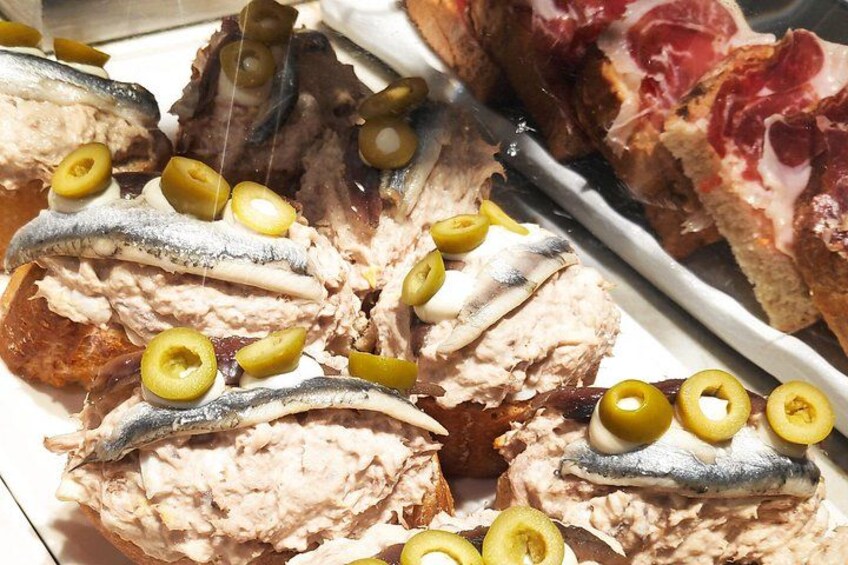 Sliced fish topped with olives, bread, and a piece of meat. 5