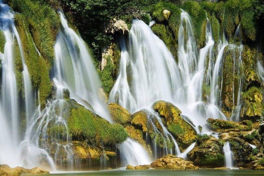 Een meerlaagse waterval met stromend water over met mos begroeide rotsen. 4