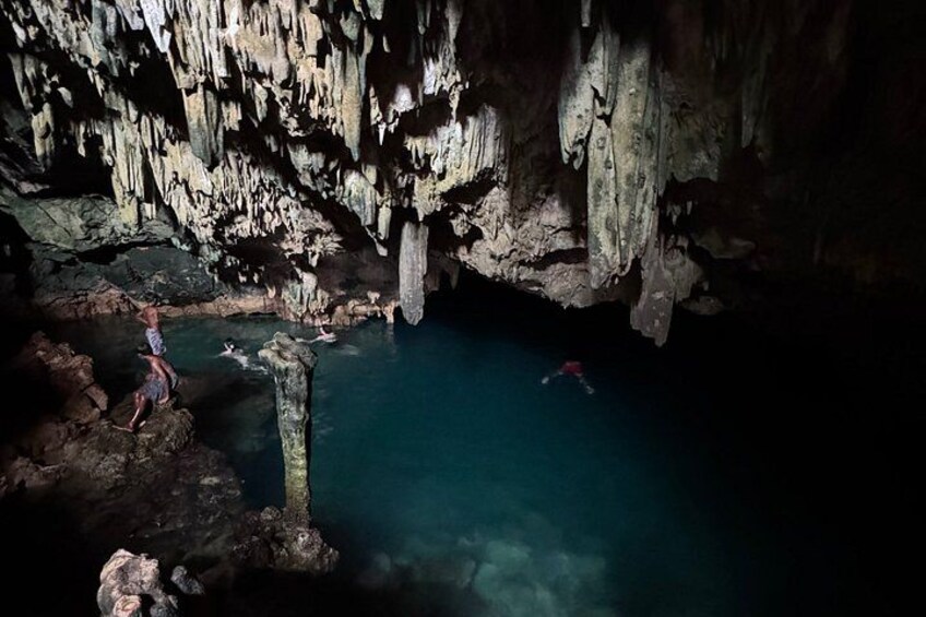 Une grotte ornée de stalactites et de stalagmites, un bassin aux eaux cristallines et une personne qui nage. 4
