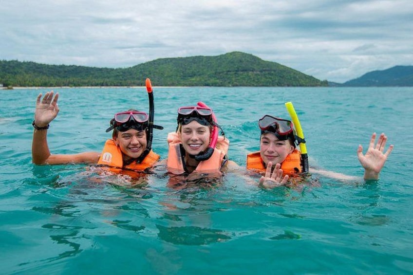 Three people snorkeling in clear blue water with a hilly landscape in the background. 1
