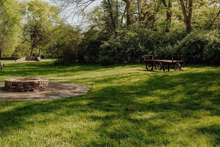 A park with a stone fire pit, a wooden bench, and lush green grass. 3