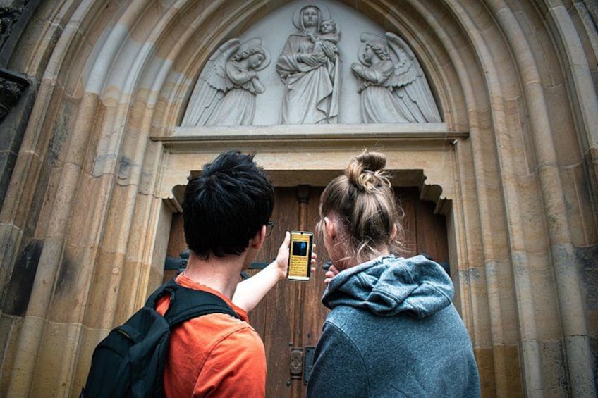 Dos personas fotografiando la entrada de un edificio con un arco labrado y estatuas en la parte superior. 5