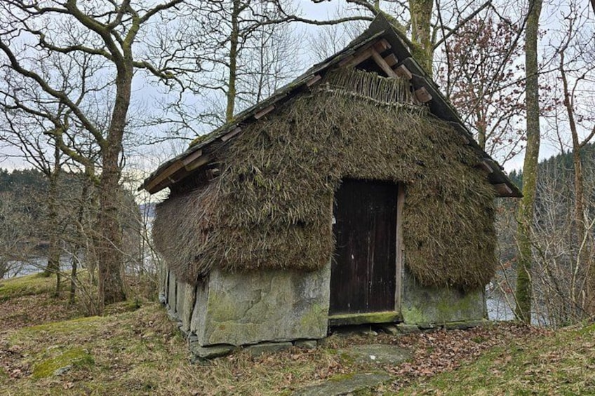 Een rieten hut met een houten deur, omringd door bomen en een waterpartij. 5