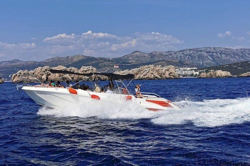 A speedboat with passengers on a clear day, water, and rocky coastline in the background. 5