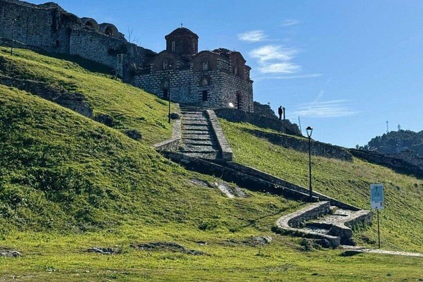 A stone staircase leading up a grassy hill towards a historic building with a bell tower. 4