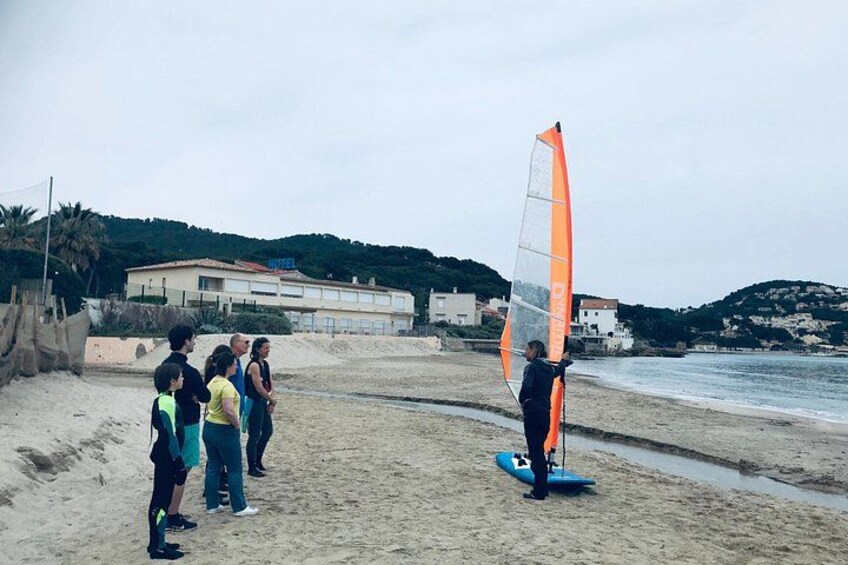 Ein Strand mit Menschen, einem Windsurfbrett und einem Hotel im Hintergrund. 3