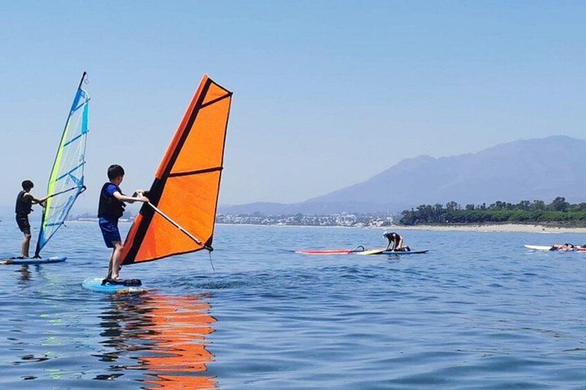 Menschen windsurfen auf ruhiger See, im Hintergrund Berge. 1