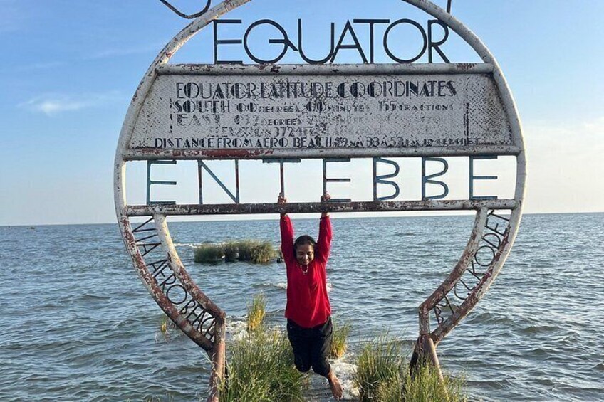 Una persona de pie bajo un letrero que dice 'Ecuador' y 'ENEBE', con agua y un cielo despejado al fondo. 2