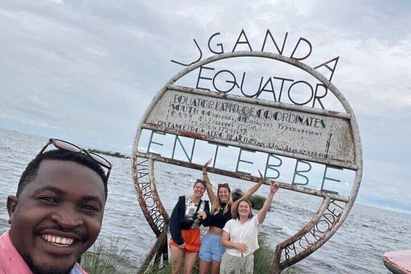 A sign with 'UGANDA EQUATOR' and 'EQUATOR SOUTH TROPIC OF CORDINATES' written on it. 1