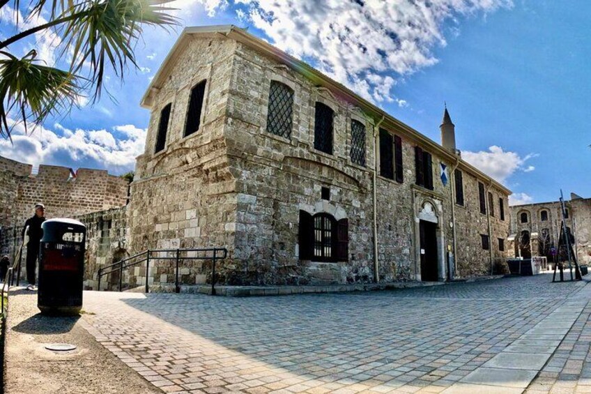 Un edificio histórico de piedra con ventanas arqueadas y una torre de campanas, rodeado de calles empedradas y palmeras. 3