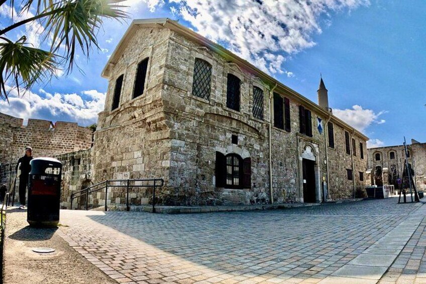 A historic stone building with a clock, a cobblestone street, and a clear blue sky. 3