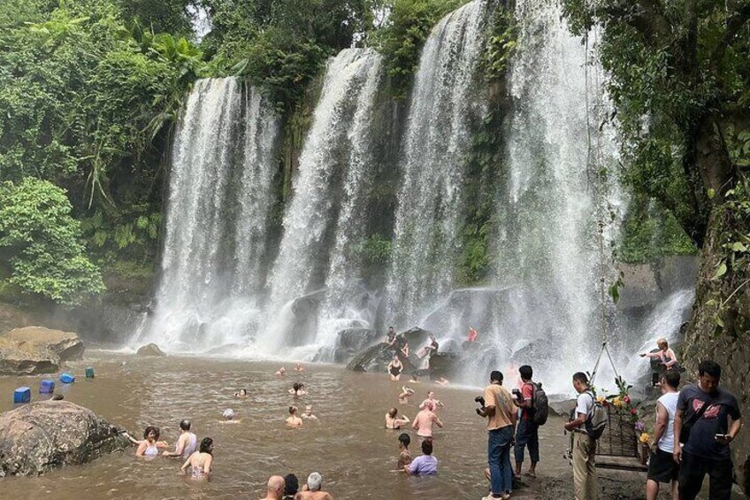 A waterfall with people swimming and standing around in the water. 5