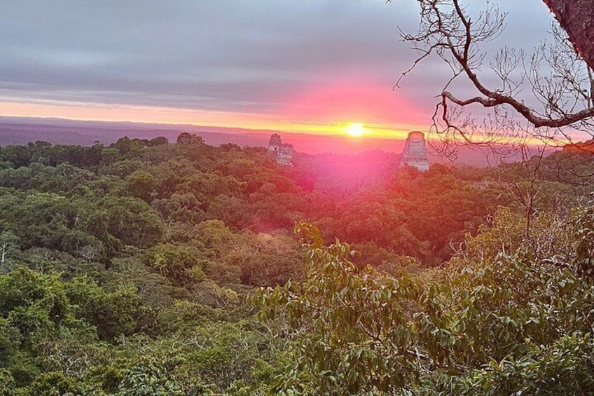 Een zonsondergang boven een dicht bos, met in de verte oude ruïnes. 3