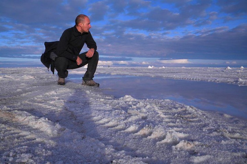A person crouching on a frozen landscape with ice formations and a cloudy sky. 1