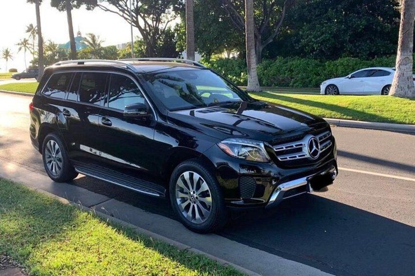 A black SUV parked on a street with grass and trees in the background. 2