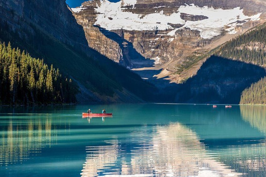 A calm lake with a canoe, surrounded by forested mountains and snow-capped peaks. 5