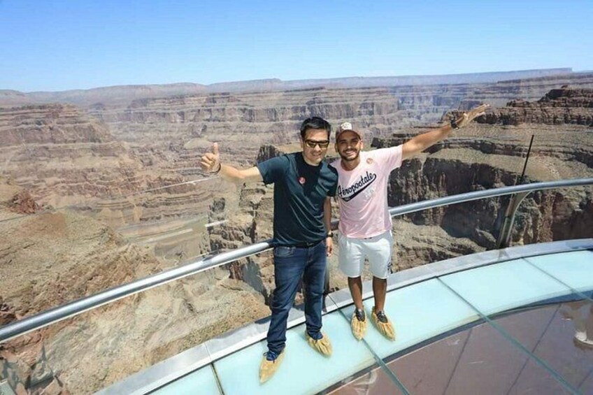 Two people standing on a glass platform with a canyon view. 3