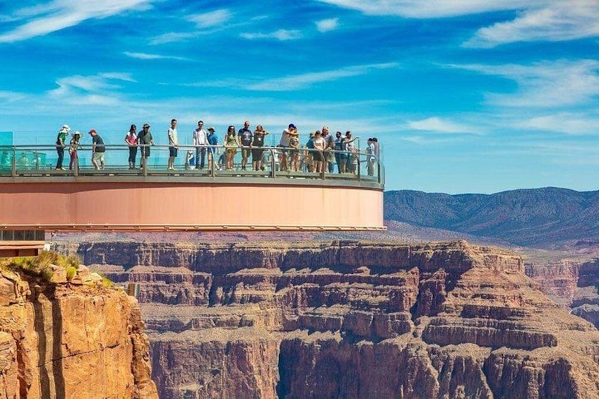 A group of people on a glass bridge over a canyon with a clear sky. 1
