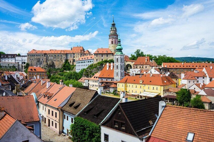 A town with historic buildings, a prominent church tower, and a castle in the background. 1
